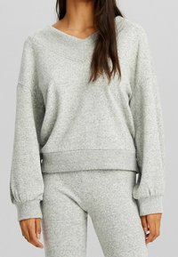 Maglione grigio, in fantasia, oversize, con scollatura a V e polsini a costine. Abbinato a pantaloni grigi coordinati, con vestibilità rilassata.