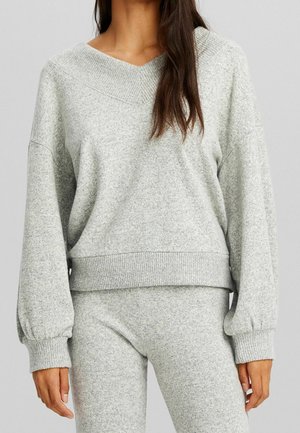 Grijze, getextureerde, oversized gebreide trui met een V-hals en geribde manchetten. Gecombineerd met bijpassende grijze broek, met een ontspannen pasvorm.