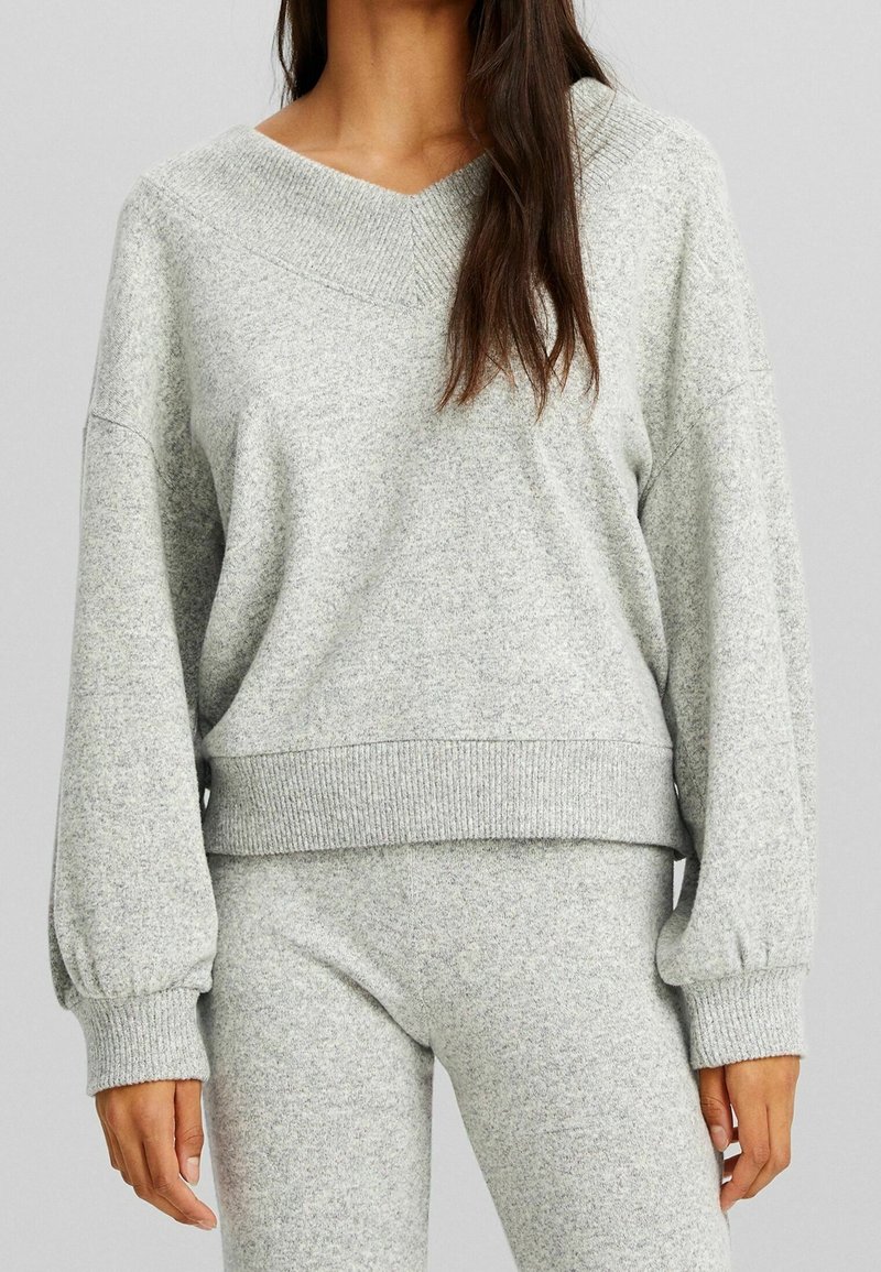 Maglione grigio, in fantasia, oversize, con scollatura a V e polsini a costine. Abbinato a pantaloni grigi coordinati, con vestibilità rilassata.