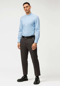 Camicia azzurro chiaro con bottoni e collo alla coreana, abbinata a pantaloni grigio scuro e scarpe nere. La camicia è liscia e aderente.