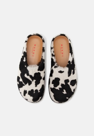 Ζευγάρι παντόφλες slip-on με ασπρόμαυρο σχέδιο αγελάδας, με ταμπά εσωτερική σόλα και κόκκινο λογότυπο Marni σε λευκό φόντο.