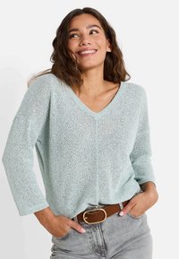 Suéter de punto azul claro con escote en V y mangas de tres cuartos. Corte holgado, con una textura intrincada y un estilo casual.