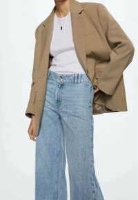 Blazer beige de gran tamaño, camiseta blanca ajustada, jeans de pierna ancha en azul claro. Tejido suave con hombros estructurados y detalles sutiles.