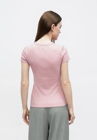 Różowy t-shirt z krótkim rękawem wykonany z miękkiej bawełny, o dopasowanym kroju i zaokrąglonym dekoltem, noszony z jasnoszarymi, wysokim stanem spodniami.