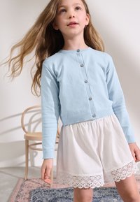 Light blue cardigan with button closure and long sleeves, paired with white textured shorts featuring a lace hem.