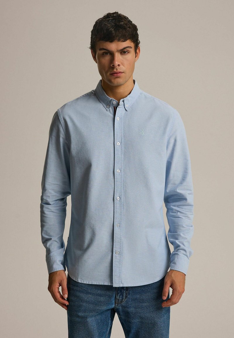 Jasnoniebieska koszula zapinana na guziki, wykonana z bawełny, z kołnierzykiem, długimi rękawami oraz haftowanym logo na piersi. Połączona z niebieskimi dżinsami.
