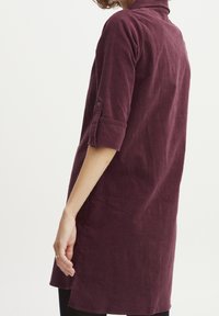 Burgundowa sukienka koszulowa z korduroy z rękawami 3/4 i zapięciem na guziki, o prostym kroju, z teksturowanym materiałem i bocznymi rozcięciami.