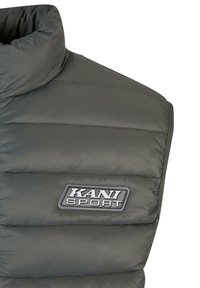 Siva pufasta jakna z visokim ovratnikom, ki ima vodoravne šive in blagovno oznako "KANI SPORT" na sprednji strani.