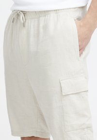 Beige cargoshorts van een lichtgewicht stof, met een elastische tailleband, zijzakken en een flapzak op de dij.