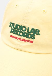 Gul bomulds baseballcap med broderet tekst i grønt og rødt: "STUDIO LAB. RECORDS" og "#BROOKLYN, NEW YORK." Flad skygge-design.