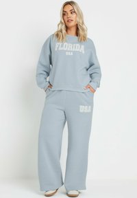 Ljusblå sweatshirt och vida byxor i en uppsättning, med "FLORIDA" och "USA" i vit text. Mjuk tyg med avslappnad passform och sidofickor.
