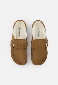 Scarpe slip-on in suede marrone con una morbida fodera in pelliccia bianca, dotate di una fibbia decorativa e dettagli cuciti lungo i bordi.