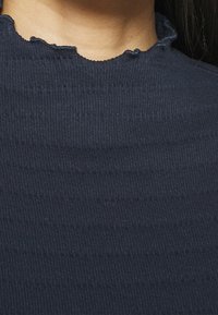 Marinblus ribbad topp med en texturerad yta och slitna kanter. Har horisontella ränder och en åtsittande design.