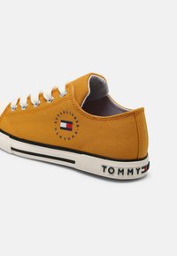 Gula canvas sneakers med vita snörningar, rund tå och svarta accenter. Har en logotyp patch och "TOMMY" text på hälen.