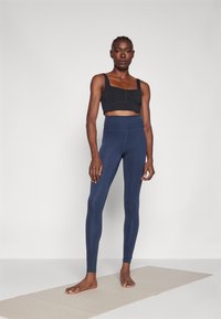 Μαύρο αθλητικό σουτιέν με τετράγωνη λαιμόκοψη, συνδυασμένο με ψηλόμεσο, αδιαφανές ναυτικό κολάν; λείο υλικό και εφαρμοστό σχέδιο.