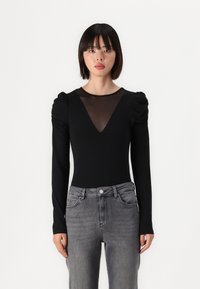 Black bodysuit with long sleeves, ruched shoulders, and a sheer mesh V-neck. Paired with high-waisted gray jeans. Smooth texture overall.