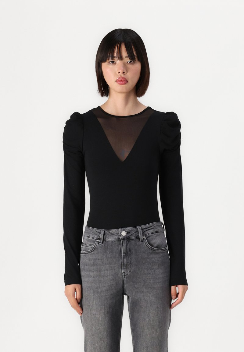 Black bodysuit with long sleeves, ruched shoulders, and a sheer mesh V-neck. Paired with high-waisted gray jeans. Smooth texture overall.