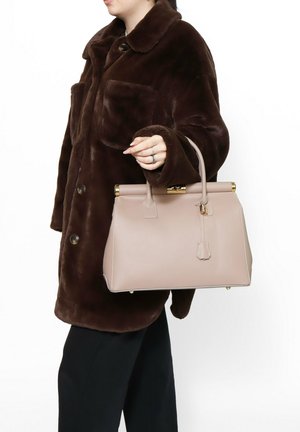 Sac à main en cuir beige avec une forme structurée, des accessoires en ton doré et une anses supérieure. Porté avec un manteau en fourrure marron.