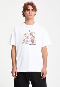 Hvid bomulds t-shirt med et farverigt grafik, der viser fire tegneserieansigtter samt teksten "CHOMP CHOMP" og "VOLCOM" nederst.