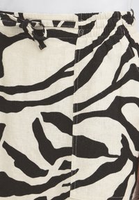 Zone de la taille d'un pantalon à rayures zébrées noires et blanches avec une ceinture élastique et une boucle de ceinture en tissu nouée.