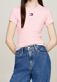 Pink ribbed short-sleeve t-shirt with a small "Tommy Jeans" logo on the chest, paired with high-waisted blue denim jeans.