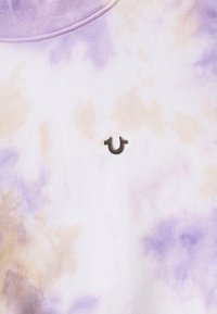 Batikfärgad sweatshirt i vitt, lavendel och beige med mjuk textur; har en liten, präglad mörk logga framtill.