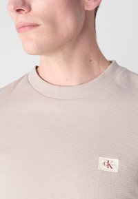 Beige bomull crewneck sweatshirt med en teksturert ribbet mønster og en liten Calvin Klein logoetikett på brystet, rund hals.