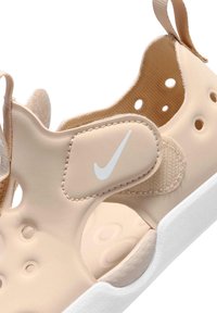 Μπεζ σανδάλι Nike με λευκή σόλα, ρυθμιζόμενο λουράκι με βέλκρο, κυκλικές οπές αερισμού και ταινίες τράβηγματος στη φτέρνα και στη γλώσσα.