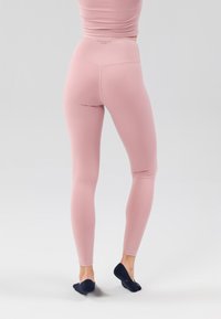 Leggings roses à taille haute et coupe ajustée, fabriqués en matériau lisse et extensible. Présentent un logo discret sur la ceinture.
