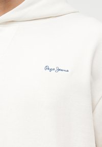 Λευκό φούτερ με κουκούλα με μπλε κεντημένο λογότυπο "Pepe Jeans" στο αριστερό στήθος, εμφανιζόμενο σε κοντινή λήψη του άνω κορμού.