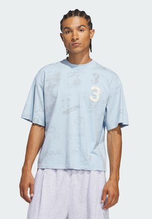 Mand med fletninger bærer en lyseblå oversized T-shirt med trykte logoer og nummer 3, kombineret med lysegrå shorts mod hvid baggrund.