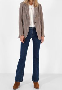 Brun houndstooth-blazer med spetsig krage, vit skjorta och mörkblå utsvängda jeans. Bärs med tanfärgade ankelkängor.