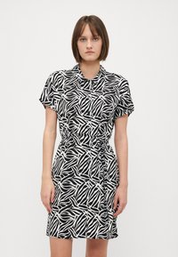 Kratka crna haljina s bijelim apstraktnim uzorkom, s gumbima sprijeda i uvučenim strukom, napravljena od lagane tkanine.