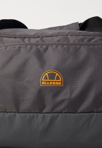 Sac en nylon gris avec une surface texturée. Doté d'un logo orange "ELLESSE" et d'un panneau inférieur lisse. Bretelles noires ajustables en haut.