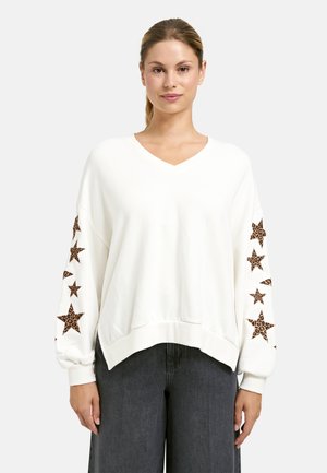 Weißer V-Ausschnitt-Sweatshirt mit Leopardenmuster-Sternapplikationen an den Ärmeln, lockere Passform und gerippte Bündchen. Kombiniert mit dunkelgrauen weit geschnittenen Hosen.