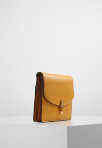 Borsa a tracolla gialla in pelle con chiusura a pattina, dotata di una fibbia metallica, bordi scuri a contrasto e una texture liscia. Design strutturato.