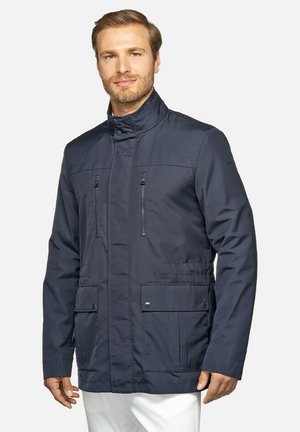 Marineblauwe waterdichte jas met een hoge kraag, ritszakken op de borst, drukknoopvoorzakken en een gladde textuur. Gepersonaliseerde pasvorm voor warmte.
