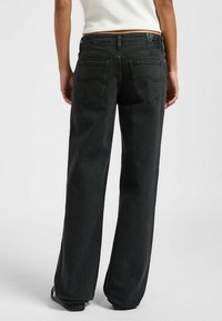 Jeans anchos negros de mezclilla, con una cintura alta, bolsillos traseros con costura curva y una etiqueta de la marca en la parte trasera de la cintura.