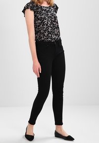 Svart blommig blus med korta volangärmar, kombinerad med svarta tajta jeans och platta svarta skor. Avslappnad outfit som framhäver blommiga mönster.