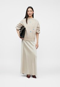 Beige knitted sweater with blue hearts, paired with a long light-colored skirt. Model holds a black handbag, wearing burgundy heels.