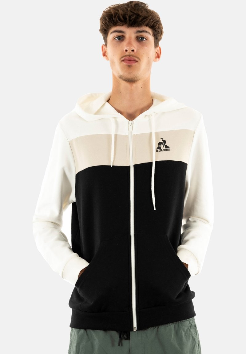 Felpa con zip in bianco e nero con pannello centrale beige. Presenta tasche a marsupio, cappuccio con lacci e logo sul lato sinistro.