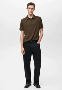 Hnědý polo tričko s krátkými rukávy, volný střih, spárované s černými kalhotami rovného střihu a černými botami. Jednoduchý design, bez viditelných vzorů nebo akcentů.