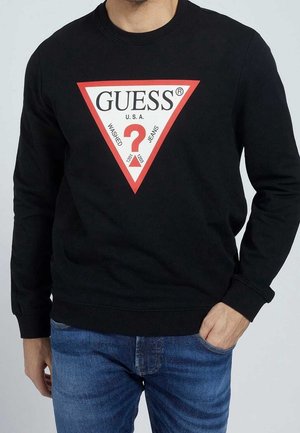 Felpa nera con un logo triangolare rosso che riporta il testo "GUESS" e un punto interrogativo. Maniche lunghe e dettagli a costine sui polsini.