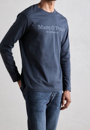 T-shirt manches longues bleu marine avec col rond, imprimé "Marc O'Polo EST. IN STOCKHOLM" en gris clair. Porté avec un jean stone wash.