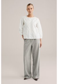 Witte geborduurde blouse met lange mouwen, knoopsluiting en ingewikkelde bloemmotieven, gecombineerd met hoog getailleerde, grijs gestreepte brede pijpen broek.