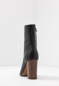 Black ankle boot made of textured leather, featuring a rounded toe and a brown wooden heel. Side zipper detail adds functionality.