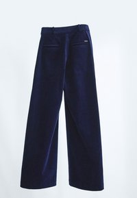 Pantalons larges bleu marine suspendus, dotés de passants de ceinture et de deux poches arrière horizontales avec une petite étiquette métallique sur la poche de droite.