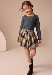 Maglia grigia a maniche lunghe abbinata a una gonna a quadri gonfia con tonalità di blu, giallo e marrone, indossata con stivali neri e calzini color crema.