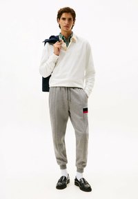Camisa polo de manga larga blanca con cuello, pantalones jogger grises con una franja roja y negra, y mocasines negros.