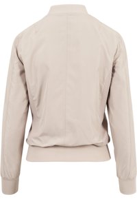 Veste bomber beige clair avec col et poignets côtelés, panneaux latéraux texturés et finition en tissu lisse.